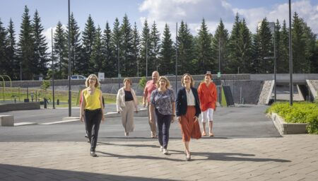 Kuusi aikuista kävelemässä hymyillen kameraa kohti